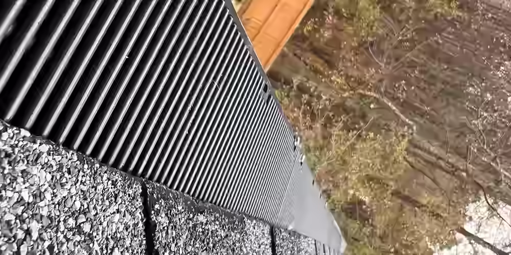Close-up field photo of black RainDrop Pro gutter guard installed along an asphalt-shingle roof edge