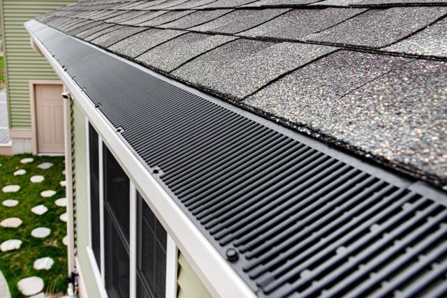 Close-up manufacturer photo of black RainDrop Pro gutter guard installed at the roof edge beneath asphalt shingles